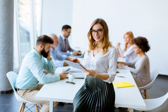 Young attractive female manager working on digital tablet while standing in modern office