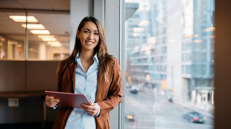 Portrait of happy businesswoman with touchpad in office looking at camera.